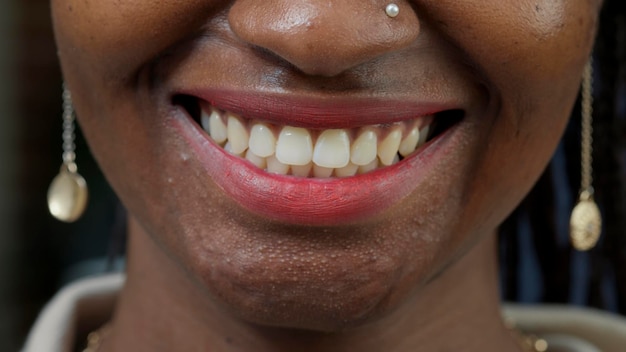 Macro shot of female model showing candid smile on camera, wearing red glossy lipstick. Young woman smiling and having positive facial expression, showing authentic emotion. Close up.