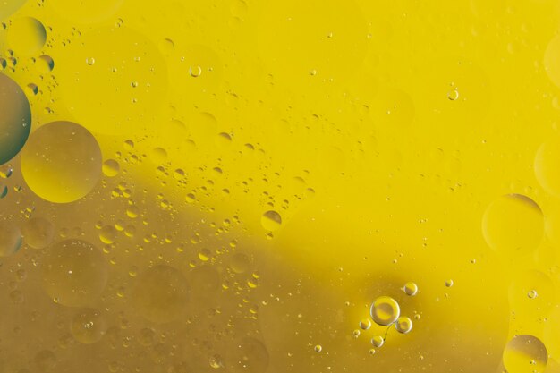 Макросъемка масла, смешанного с водой на желтом фоне