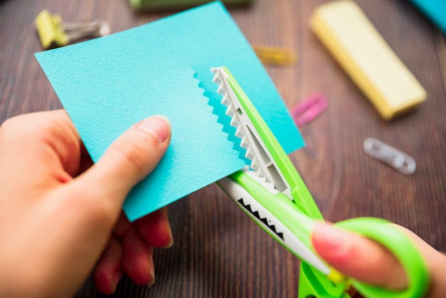 Macro shot of a person's hand cutting turquoise paper with zigzag scissor