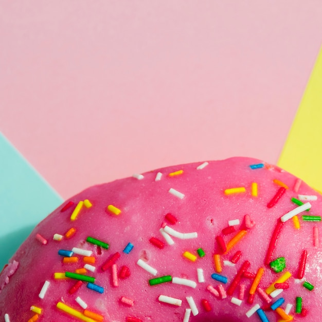 Macro shot of pink donut with colorful sprinkles on colored backdrop