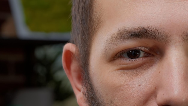 Macro shot portrait of male model showing one eye on camera, having brown eyes and smiling. Young man with authentic look and healthy vision, having positive facial expressions. Close up.