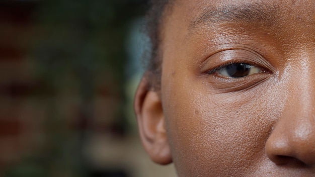 Free photo macro shot of young adult smiling and looking at camera, showing one eye and half of face. female model focusing eyesight, having eyelashes, eyebrows, pupil, retina and iris. close up.