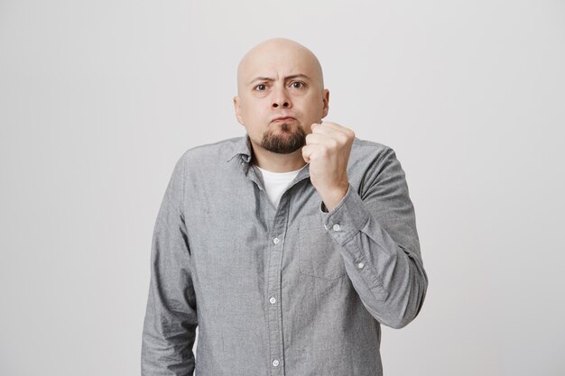 Mad bald guy showing fist, scolding or threatening