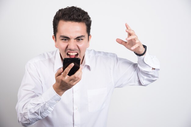 Mad businessman screaming at cellphone on white background.