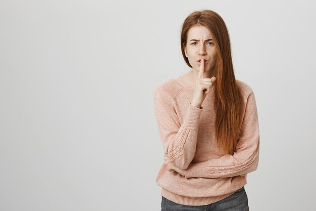 Mad redhead woman with freckles shushing with disturbed look