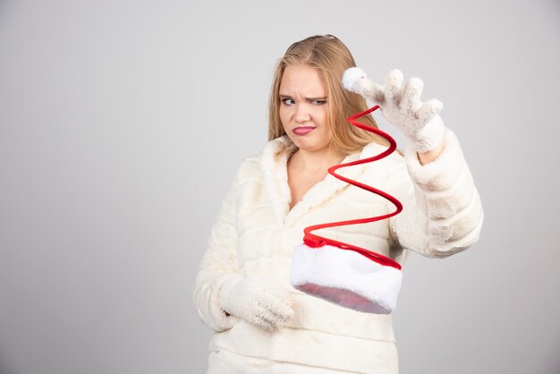 Mad woman looking at Santa hat on gray wall.