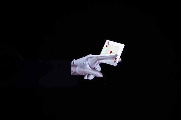 Magician holding aces playing card in fingers against black background