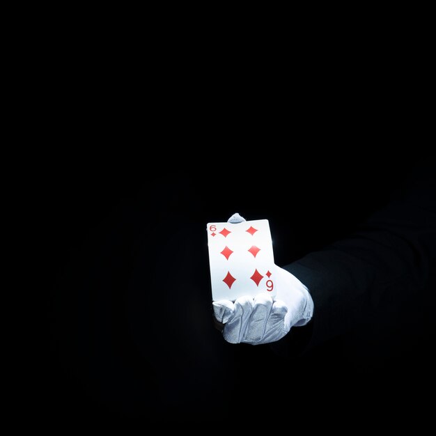 Magician's hand showing diamond playing card against black background