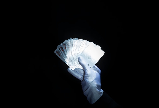Magician's hand wearing white glove holding fanned playing cards against black background