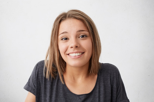 Foto gratuita magnifica bella donna con gli occhi scuri stretti e un sorriso piacevole che scrolla le spalle con un aspetto piacevole e dubbioso