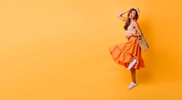 magnificent woman in long bright skirt dancing in studio. carefree inspired female model posing with pleasure on yellow.