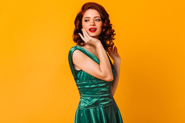 Magnificent young woman in green dress looking away Studio shot of dreamy girl isolated on yellow background