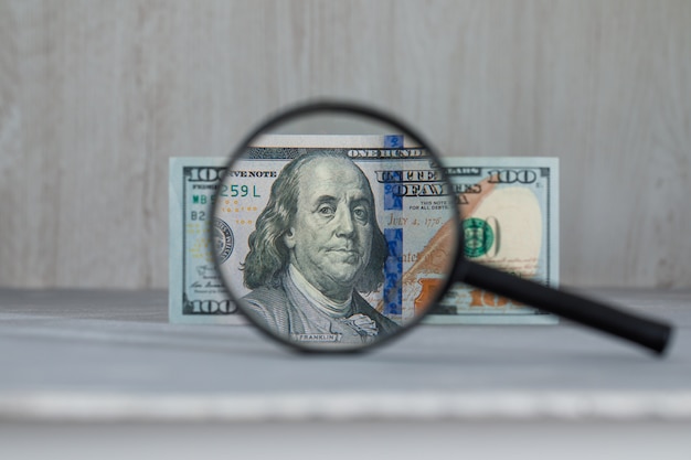 magnifying glass over dollar banknote on grey and wooden table