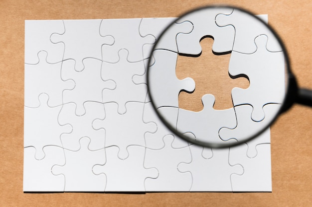 Magnifying glass on missing puzzle over brown paper textured backdrop