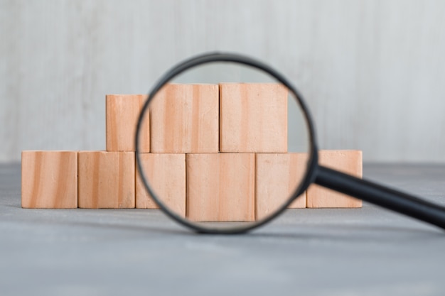 magnifying glass over wooden cubes on plaster and wooden table