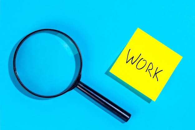 Free photo magnifying loupe and a sticker with the word work on a blue background