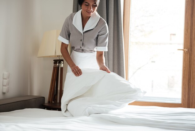 ホテルの部屋で白いベッドシートを設定するメイド