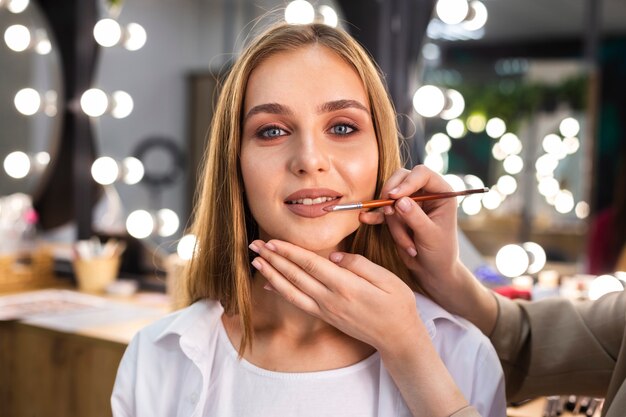 Make-up artist applying lipstick on smiling woman with brush