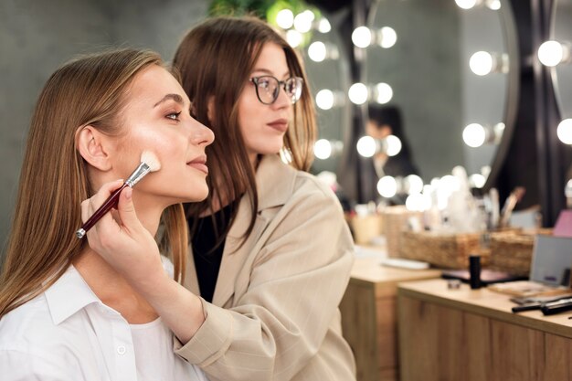 Make-up artist and woman looking at mirror applying contouring