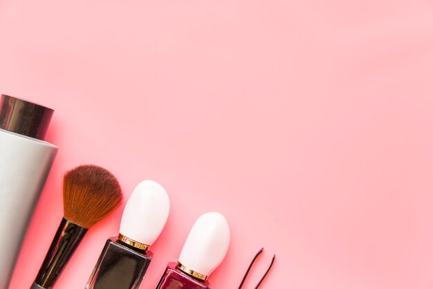 Make-up brush; cosmetics product and tweezers on pink backdrop