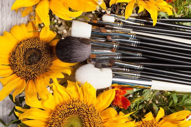 Make up brushes next to beautiful wild flowers on wooden background