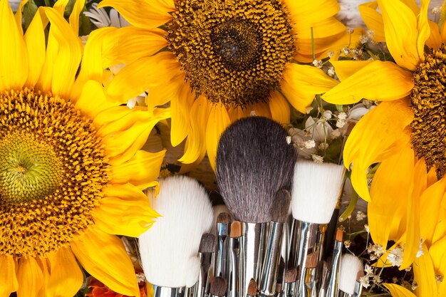 Кисти для макияжа рядом с красивыми полевыми цветами на деревянном фоне