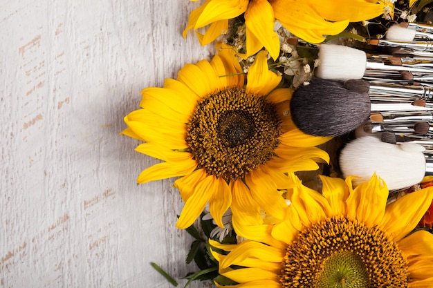 Make up brushes next to beautiful wild flowers on wooden background