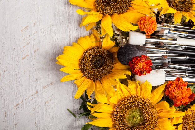 Make up brushes next to beautiful wild flowers on wooden background