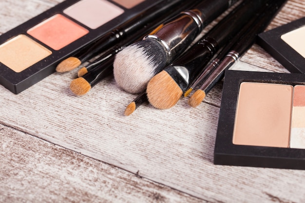 Make up brushes next to cosmetics products on wooden table in close up photo