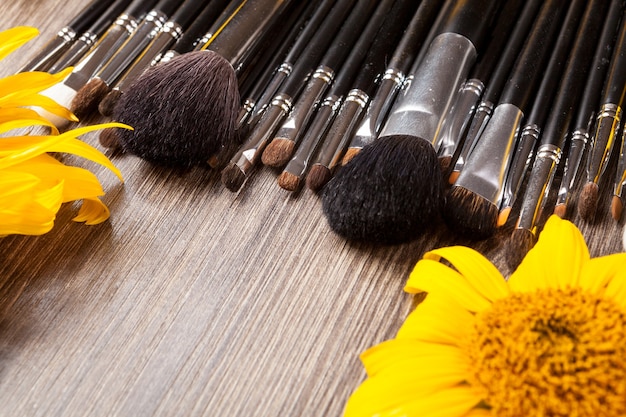 Make up brushes next to flowers on wooden background