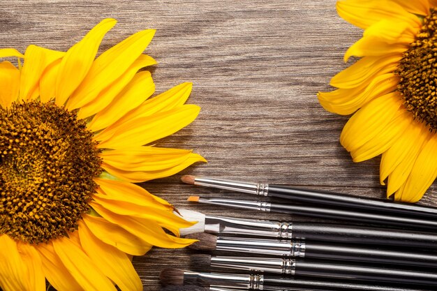 Make up brushes next to flowers on wooden background