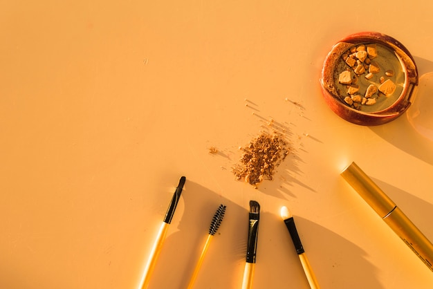 Make-up brushes; lipstick; broken face powder on dark background