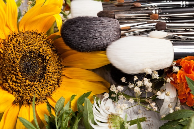 Make up brushes on a pile of wild flowers on wooden background