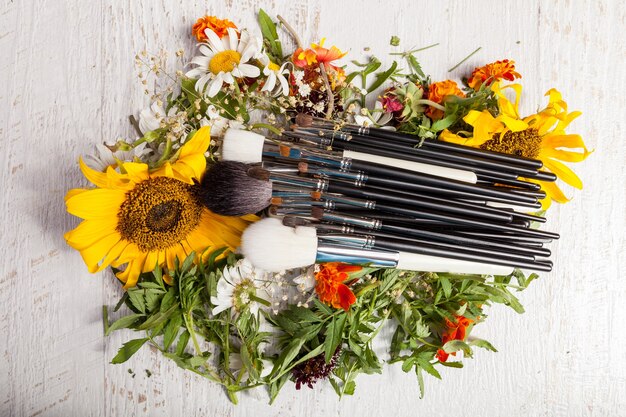 Make up brushes on a pile of wild flowers on wooden background