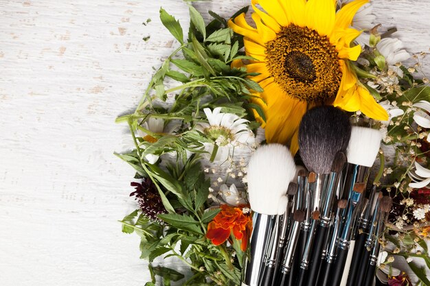 Make up brushes on a pile of wild flowers on wooden background