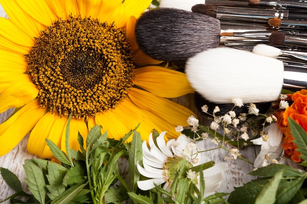 Free photo make up brushes on a pile of wild flowers on wooden background