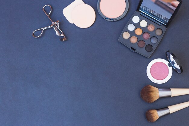 Makeup brush; sponge; blusher; eyeshadow palette and eyelash curler on blue background