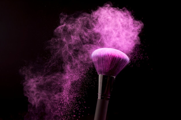 Makeup brush with purple powder dust on dark background