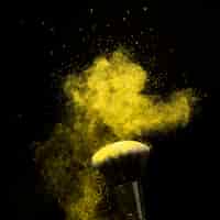 Free photo makeup brush in yellow powder dust on dark background