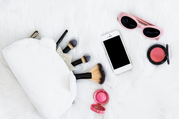 Makeup brushes in bag; mobile phone; sunglasses and pink compact face powder on white fur