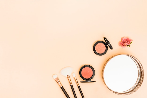 Makeup brushes; compact face powder; rose and mirror on the corner of colored backdrop