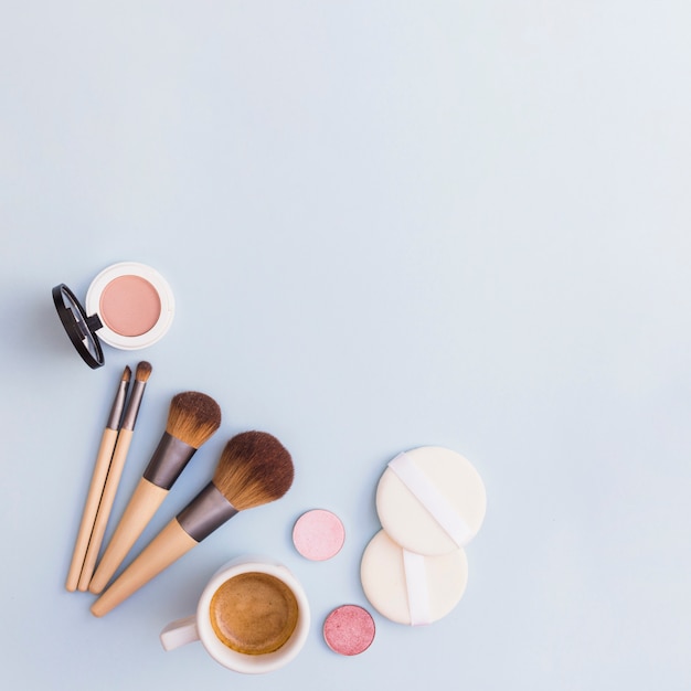 Makeup brushes; eye shadow; blusher and sponge with coffee cup on blue background