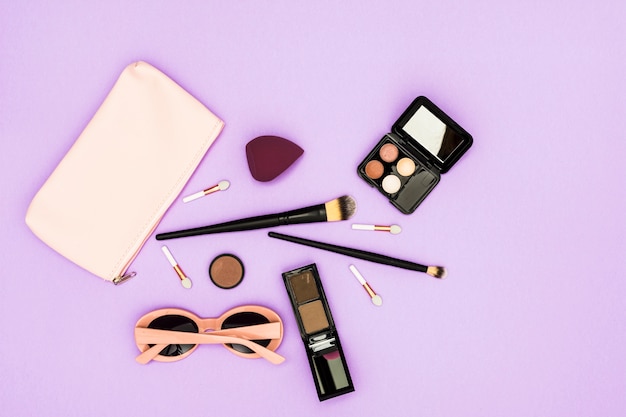Бесплатное фото Кисточки для макияжа; палитра теней и солнцезащитные очки на фиолетовом фоне