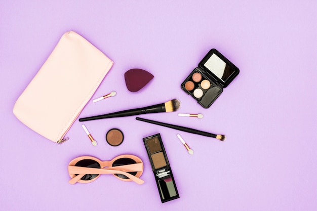 Makeup brushes; eyeshadow palette and sunglasses on purple backdrop