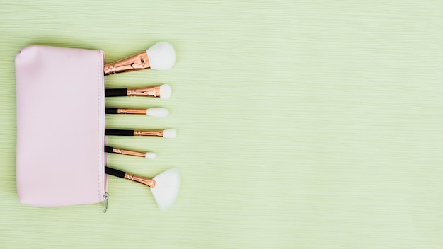 Makeup brushes inside the open bag on mint green background