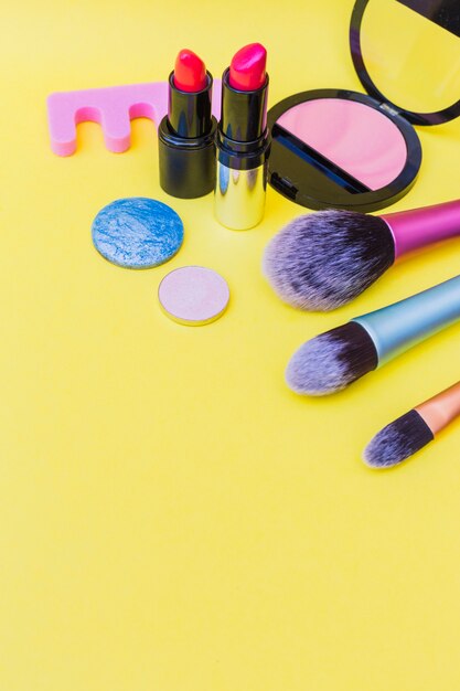 makeup brushes; lipstick; and eye shadow; pink blusher and toe divider on yellow background