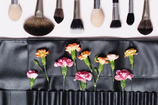Makeup brushes near carnations in bag