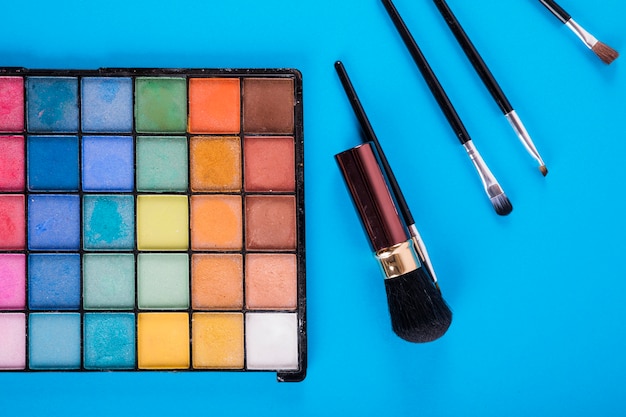 Makeup palettes with various powder colors and brushes on blue background