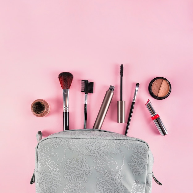Makeup products spilling out of a bag on pink background
