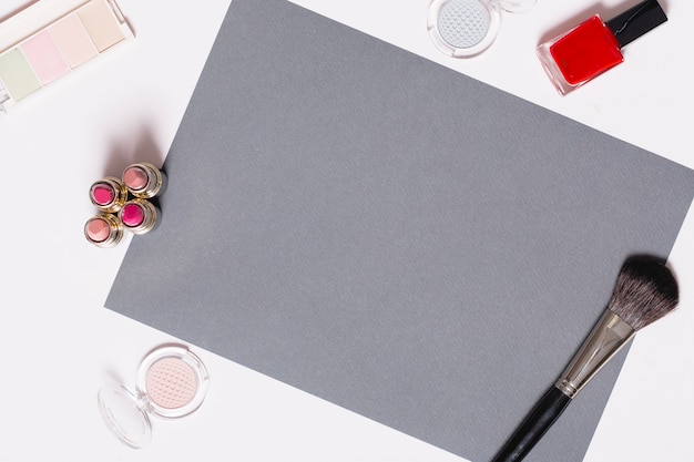 Makeup supplies around gray paper sheet